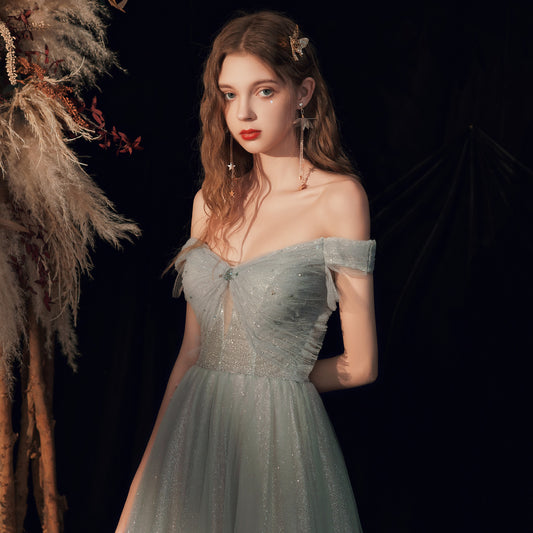 Woman in a light blue off-shoulder dress standing against a dark background with decorative elements.