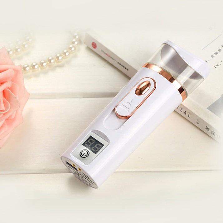 White and rose gold electronic device on a light surface with flowers and a book in the background