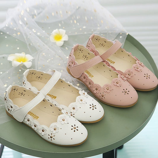 Pair of pink and white children's shoes with floral designs on a green surface.