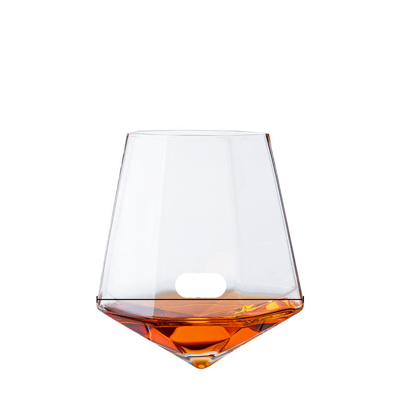 A hand holding a clear crystal wine glass with a wooden round base on a table, with ice cubes and a lime in the background.