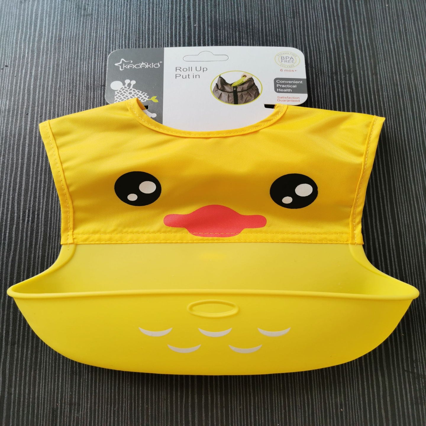 Yellow duck-shaped bib with a pink beak on a dark surface