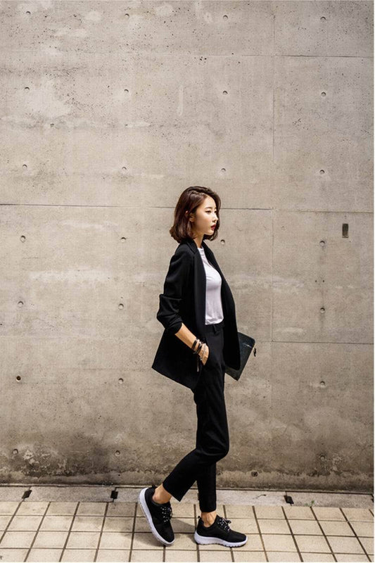 Woman in a black suit walking against a concrete wall.