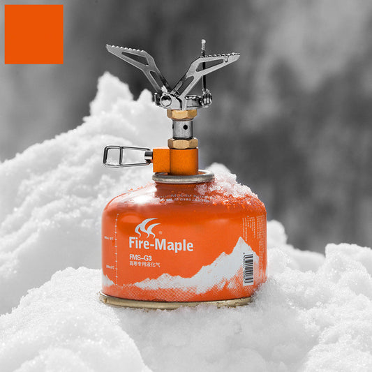 Orange camping stove with visible 'Fire-Maple' branding on a snowy background
