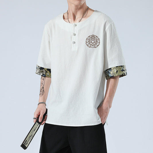 Person wearing a white shirt with floral cuffs and a mandala design, holding a belt.