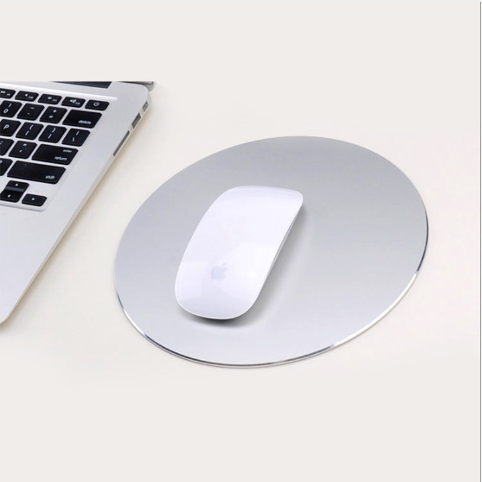 A silver aluminum alloy mouse pad on a desk with a white computer mouse on top and a laptop to the left.