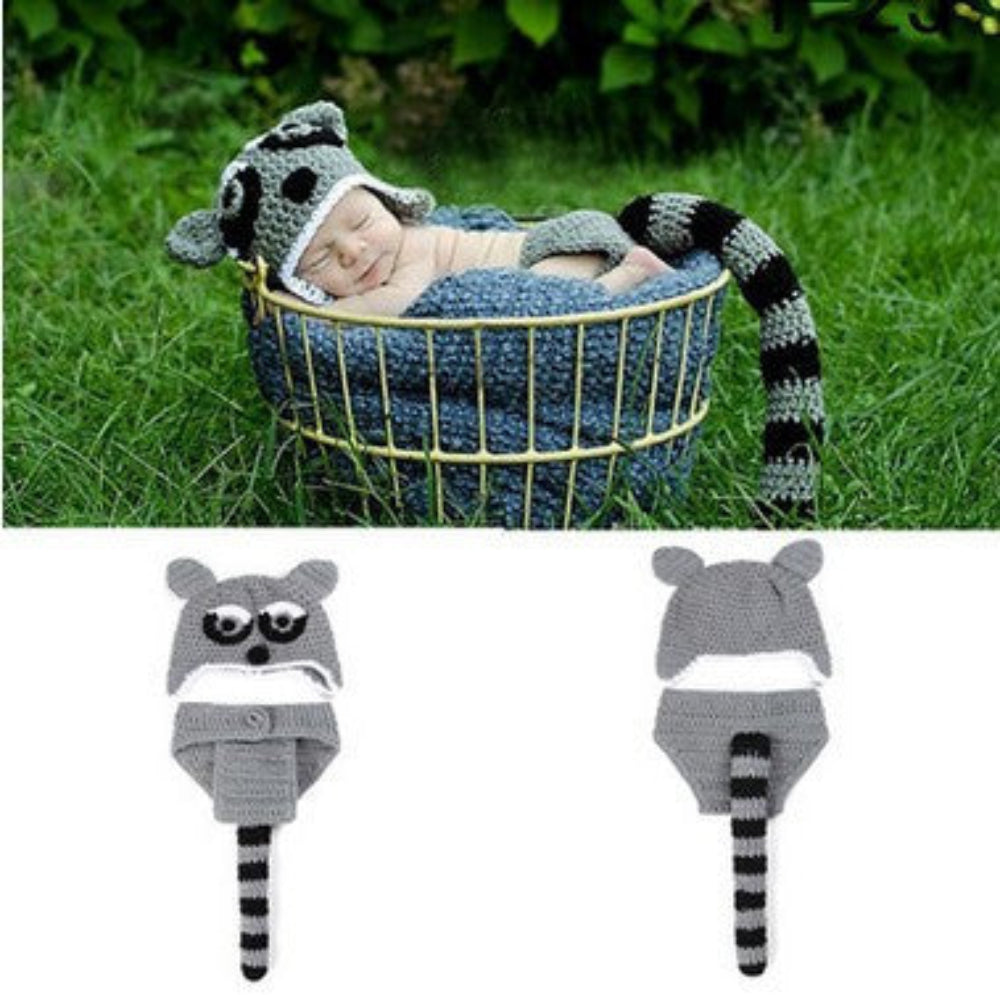 Newborn baby in a raccoon costume lying in a basket outdoors.