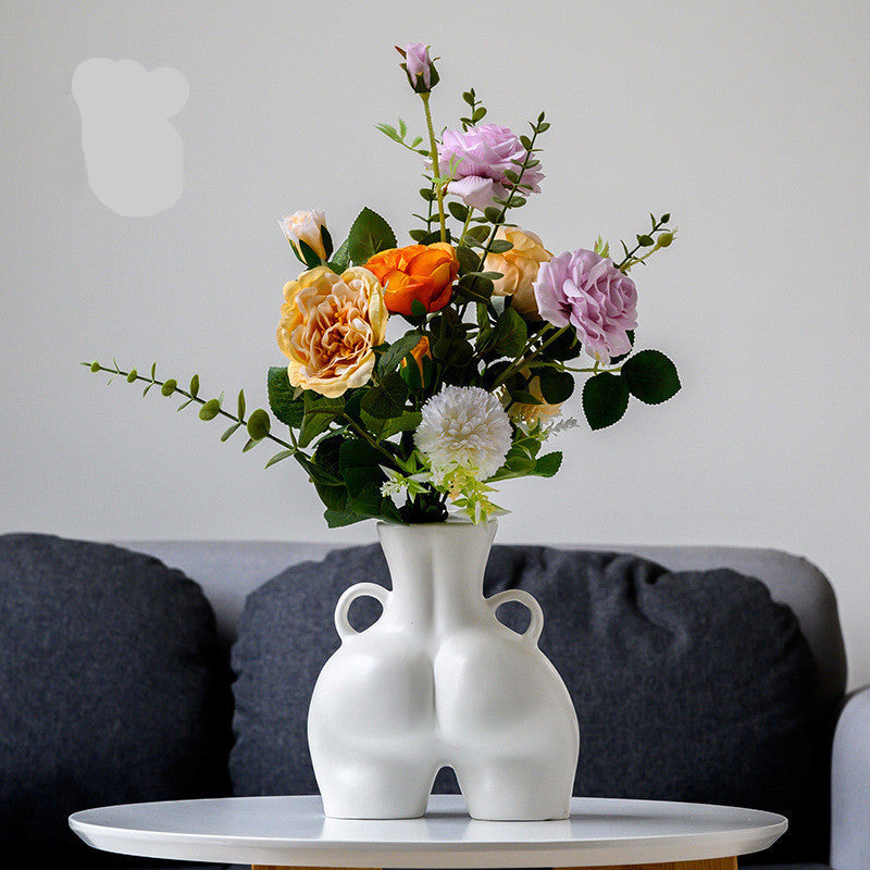 A black ceramic gourd-shaped vase on a white surface, with a bouquet of multicolored flowers arranged in it, placed against a neutral background with a grey sofa.