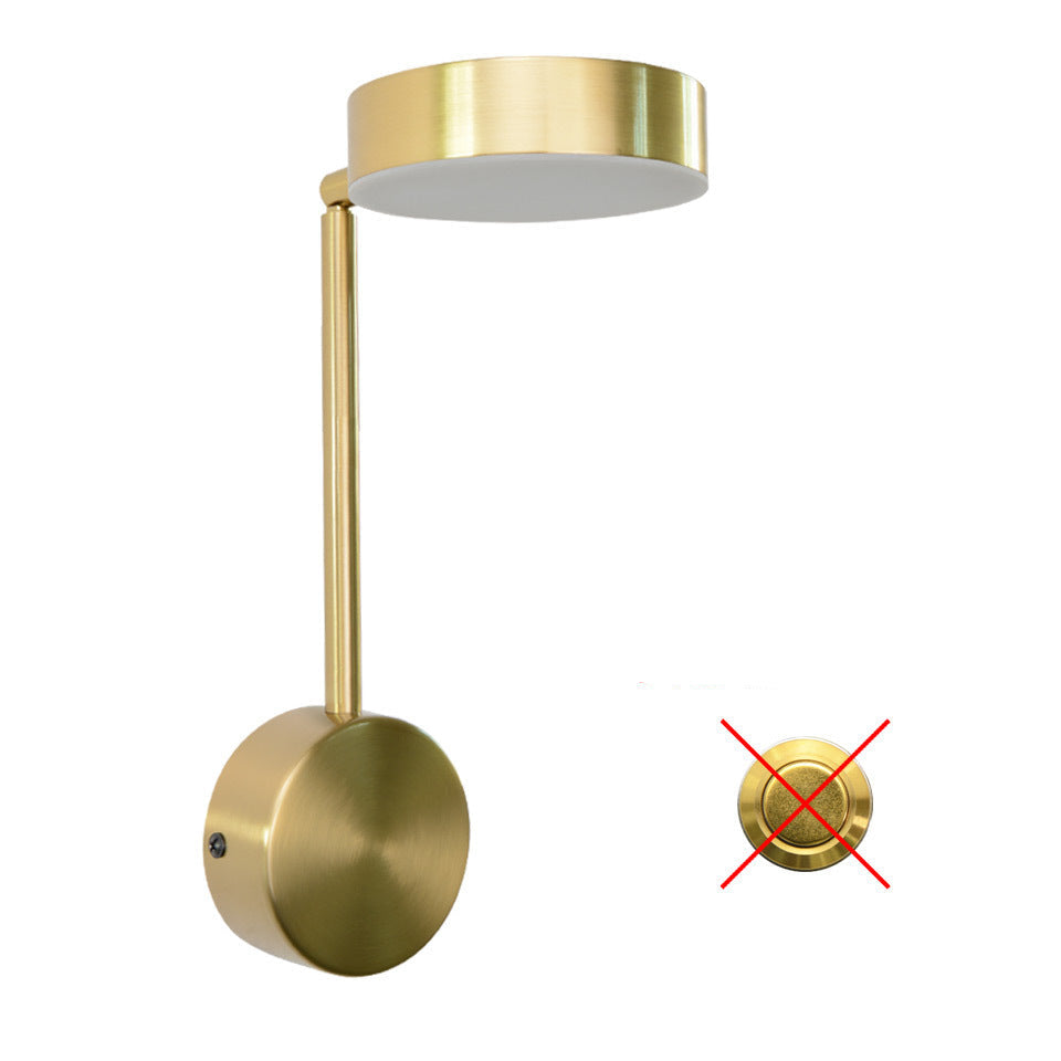 A gold-colored bedside lamp with a rotary key switch, mounted on a wall, lighting up a space with a warm glow.