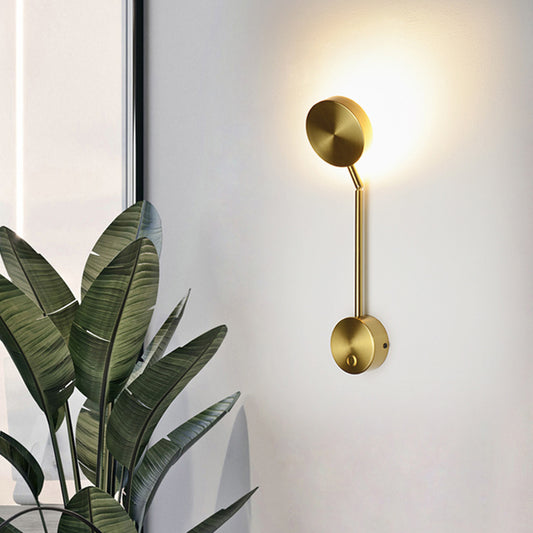 Gold wall lamp on a white wall with a plant in the foreground.