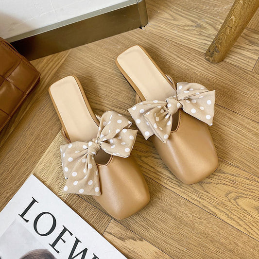 Beige sandals with polka dot bows on a wooden floor.