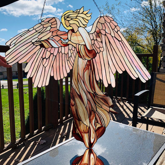 Stained glass angel sculpture on a table outdoors with a wooden deck and grassy area in the background.
