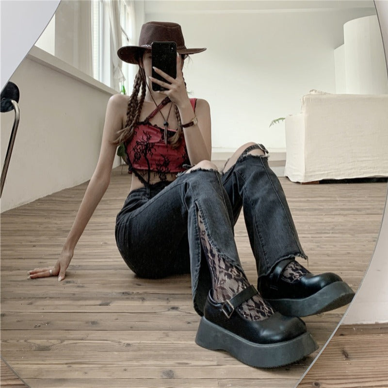 Person sitting on a wooden floor wearing black platform shoes, jeans, and a hat.