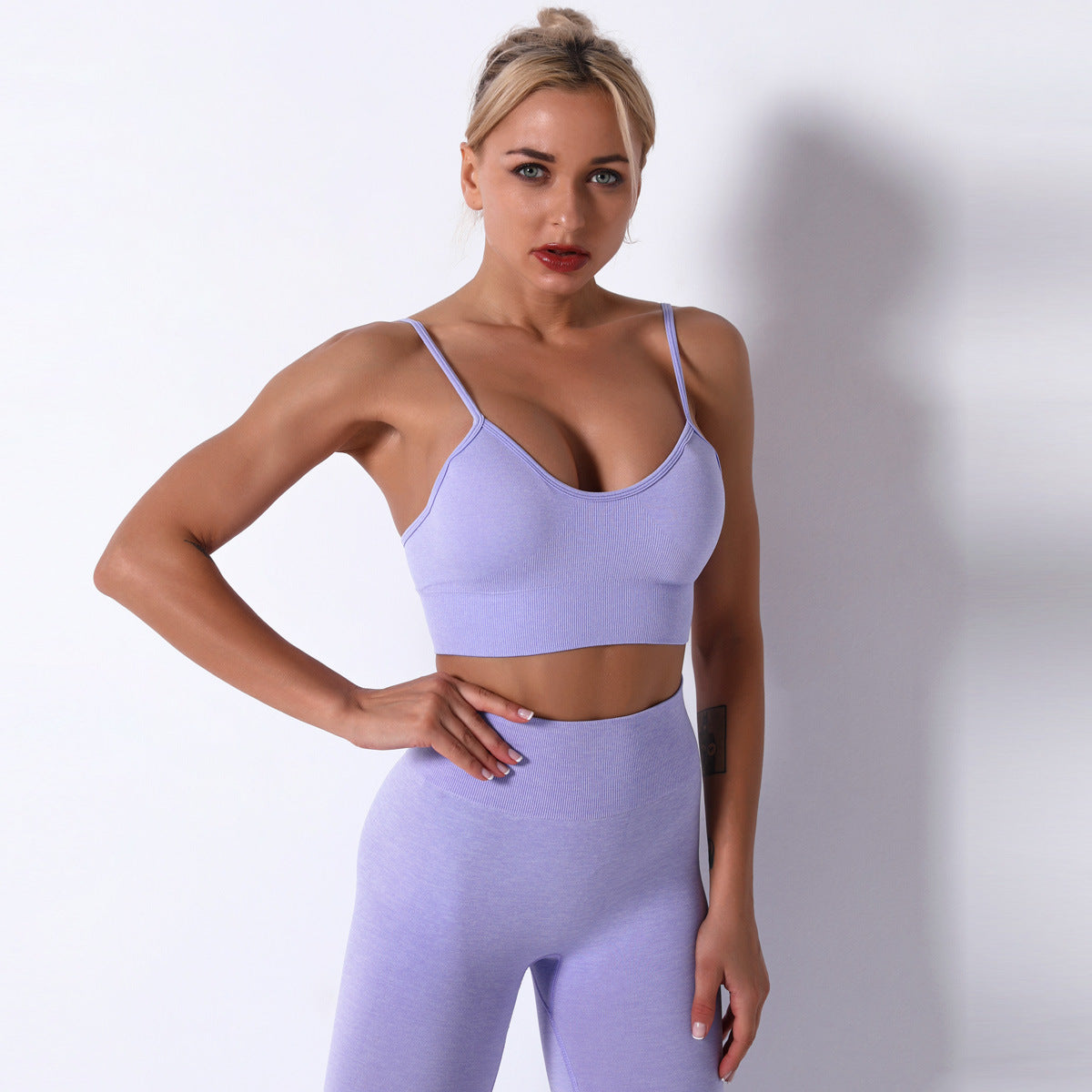 Woman wearing a light purple sports bra and leggings on a plain background