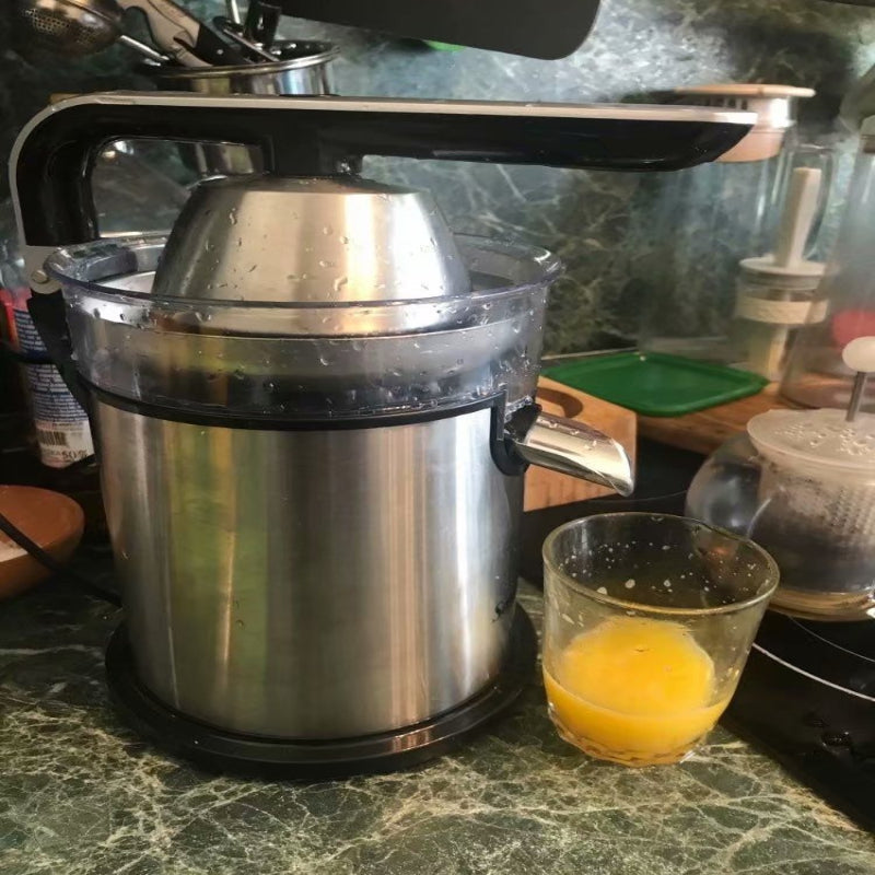 Stainless steel juicer on a kitchen counter with a glass of orange juice.