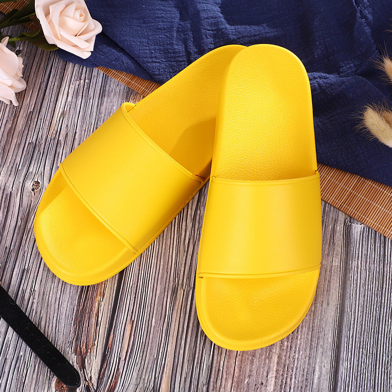 Pair of yellow slippers on a wooden surface with a blue towel and flowers in the background.