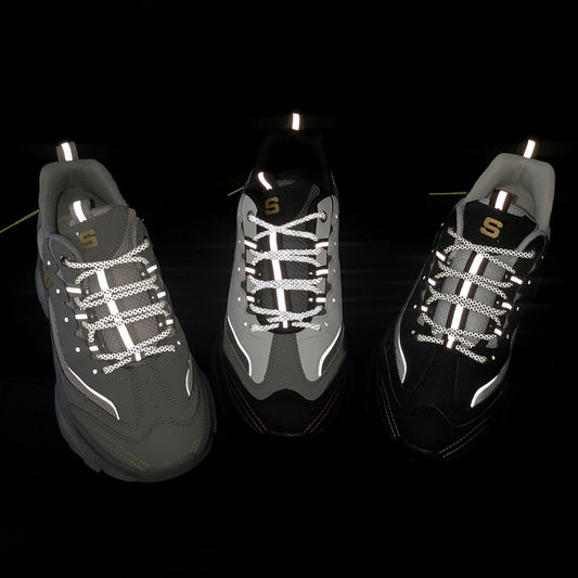 Three dark gray sneakers with reflective laces on a black background