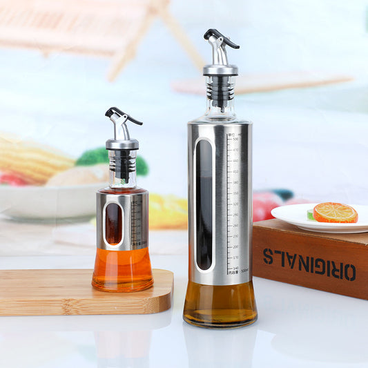 Two olive oil dispensers on a table with a blurred background of food items.