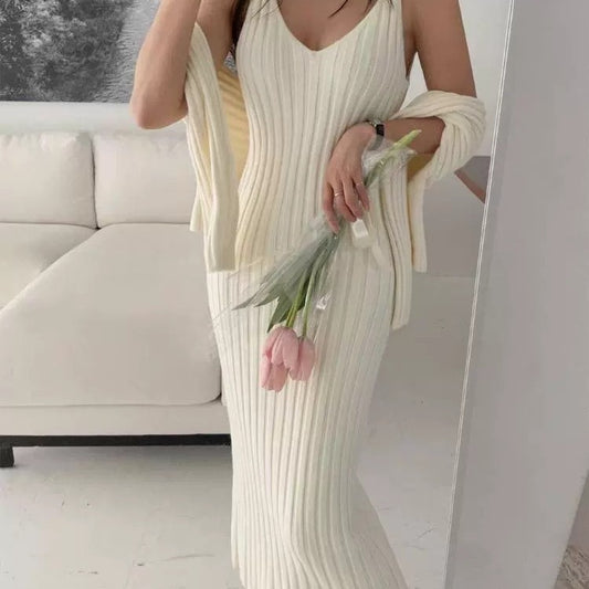 Woman in a white ribbed dress holding flowers in a room with a couch.