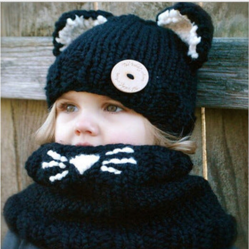 A baby wearing a beige knitted hat with a hood that has a bear face design and wooden button details.