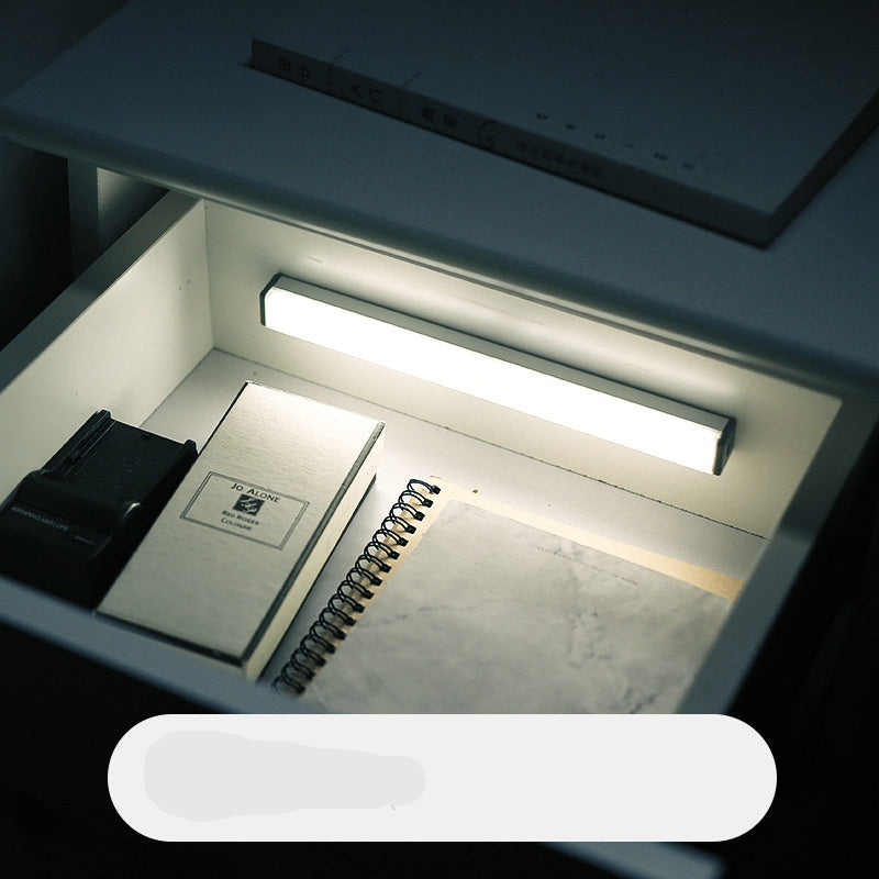Under-cabinet light illuminating a kitchen drawer with a notebook and pen inside.