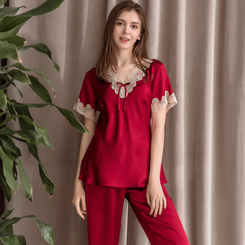 Woman wearing a red satin pajama set with lace details against a beige curtain background.