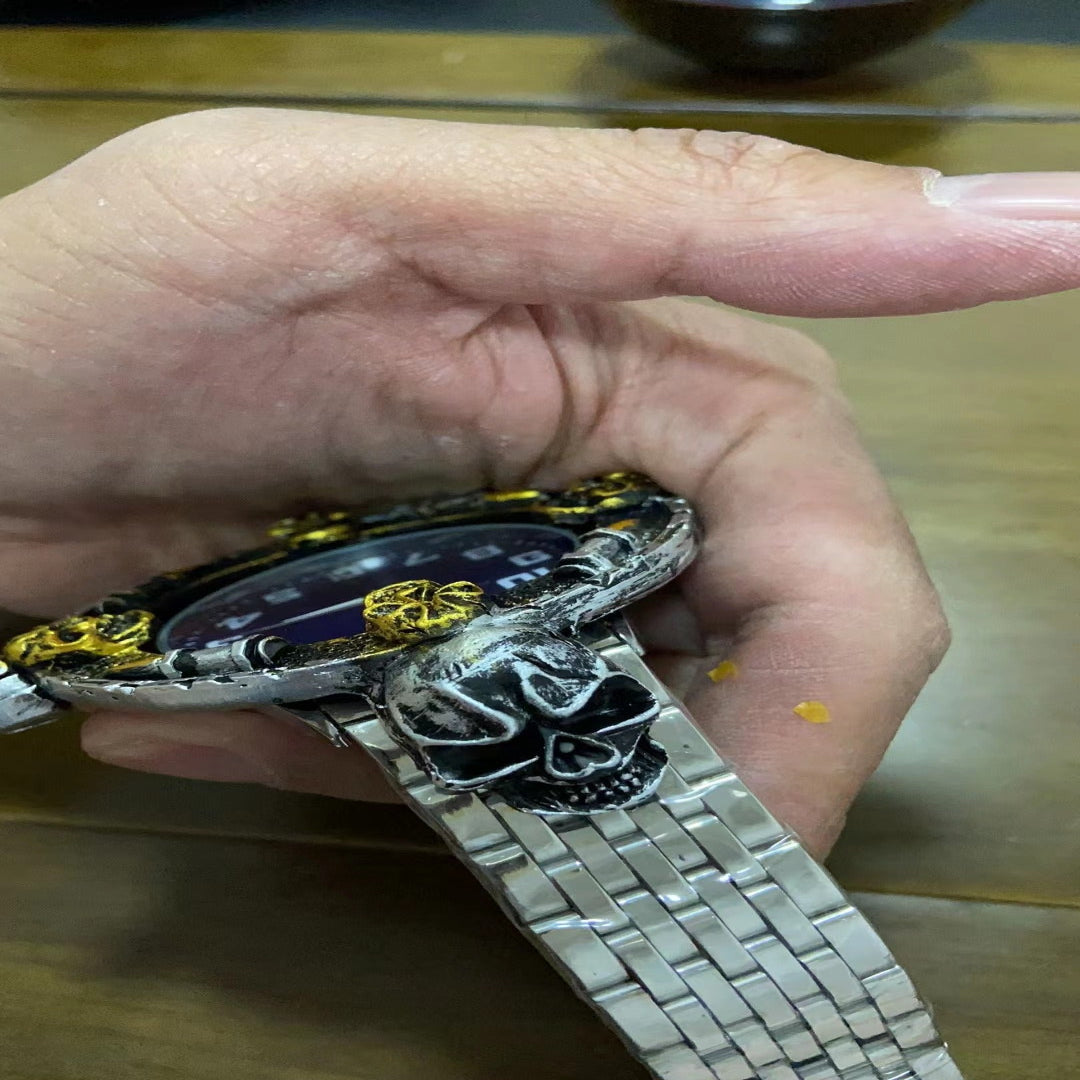 Hand holding a silver and gold watch with skull design on a wooden surface