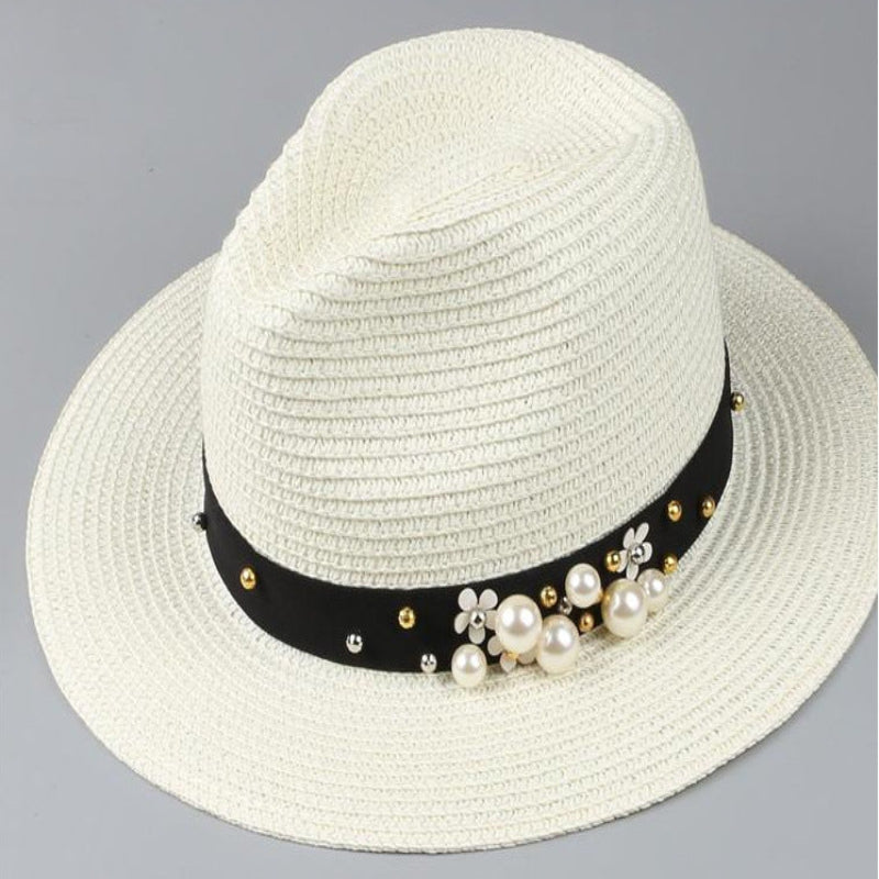 A beige panama hat with a black band placed on a flat surface, displayed against a light background with decorative items in the periphery.
