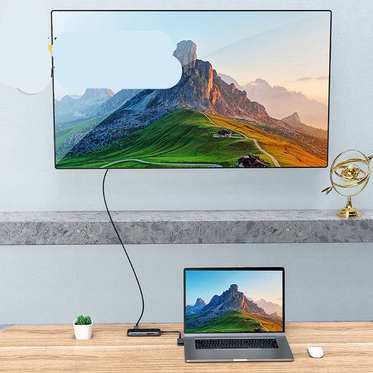 TV displaying mountain landscape with laptop on desk below.