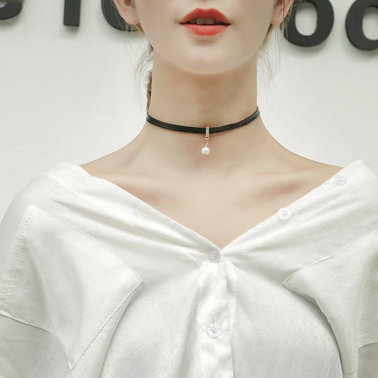 Person wearing a black choker necklace with a pearl pendant against a neutral background