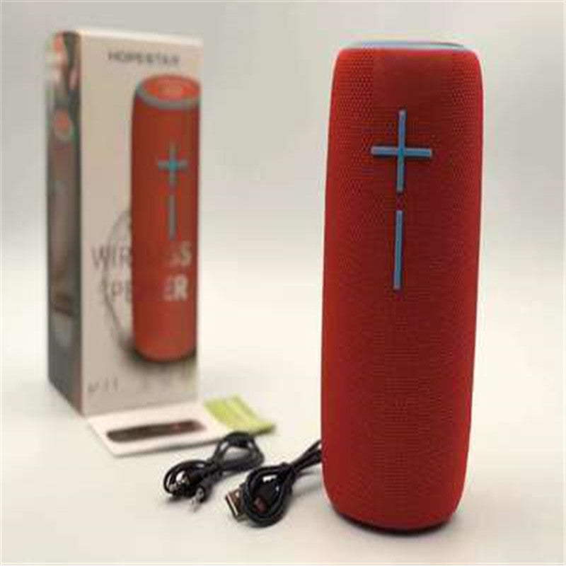 A black wireless Bluetooth speaker with a red cross design on the front, accompanied by a USB cable, a battery, and a product box.