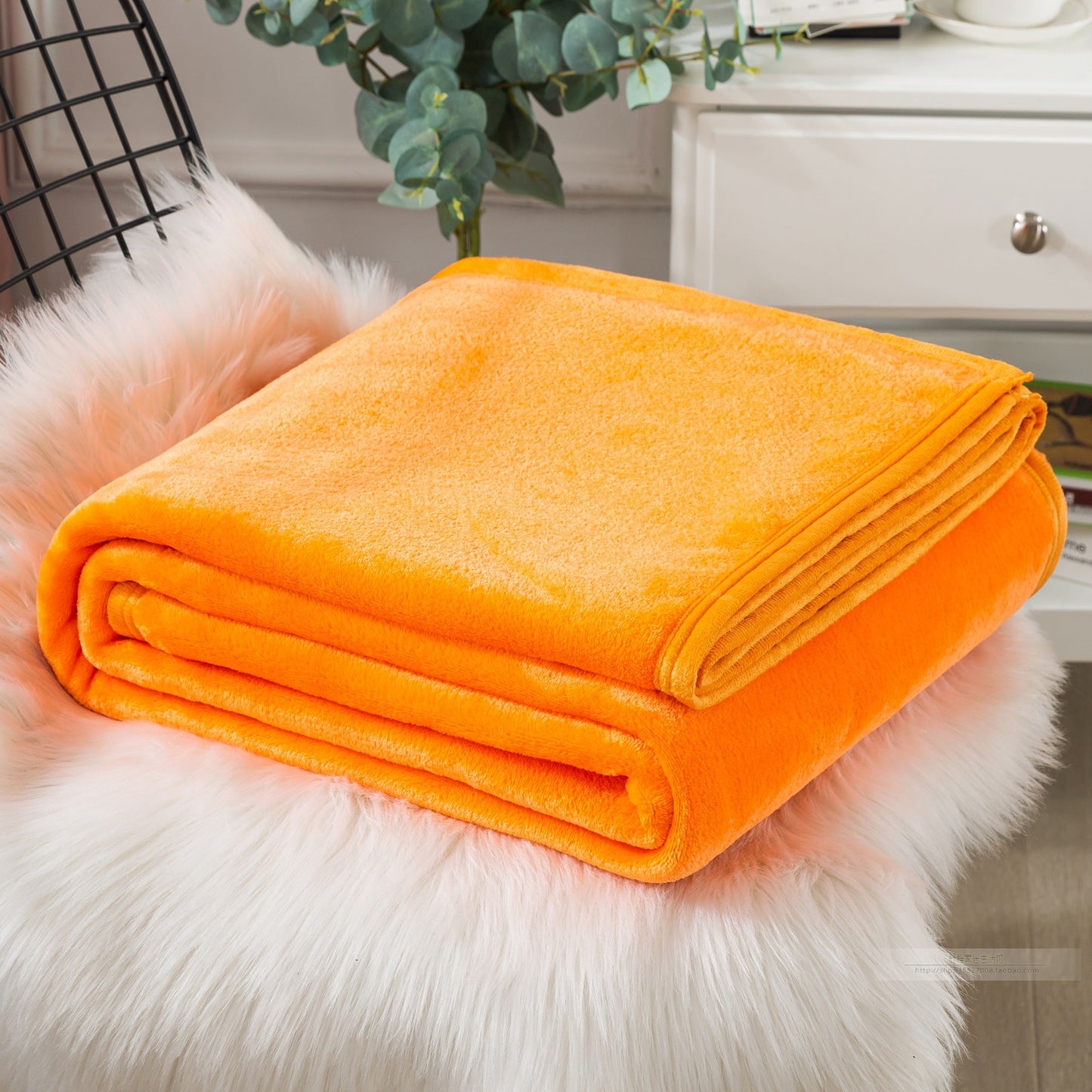 Orange blanket folded on a fluffy white surface.