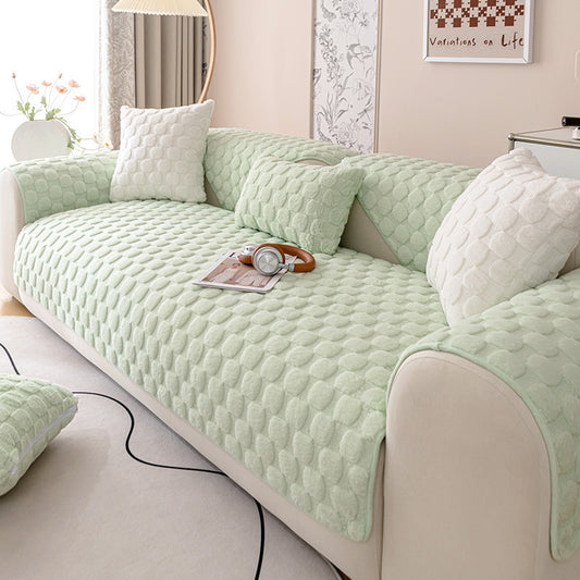 Light green quilted sofa cover on a beige sofa with decorative pillows and a magazine.