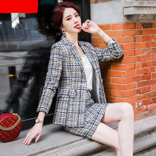 Woman in a tweed suit sitting on steps with a red bag next to her, against a brick wall.