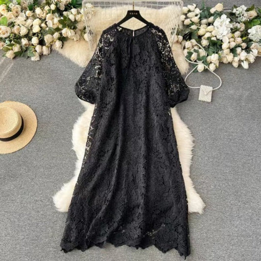Black lace dress on a hanger with flowers and a hat in the background