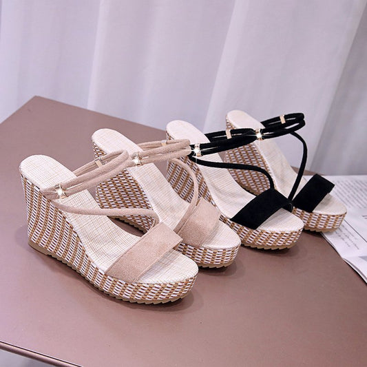 Woven wedge sandals with beige and black straps on a light pink surface.