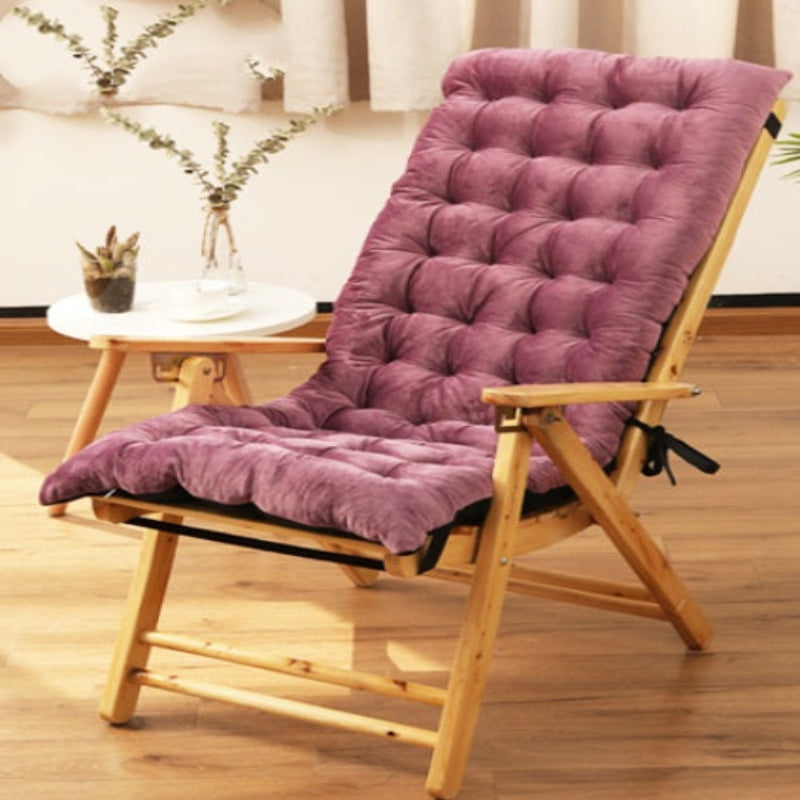 A brown chair cushion with a non-slip design placed on a wooden chair, with a small table and a plant in the background.