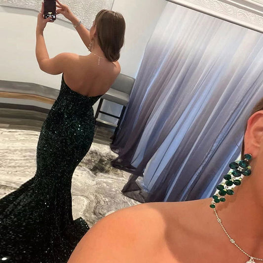 Woman in a black sequin dress taking a mirror selfie with green earrings.