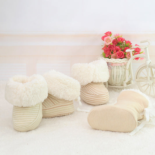 White and beige baby booties on a white surface with a basket of flowers in the background.