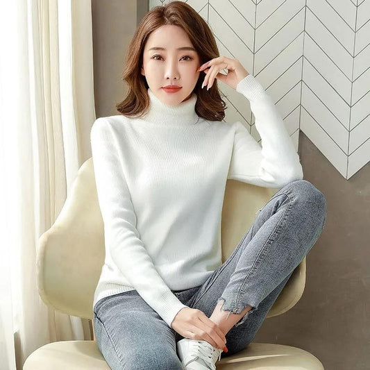 Woman wearing a white turtleneck sweater and gray jeans sitting on a beige chair.