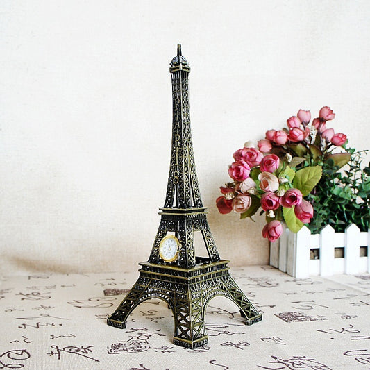 Model of the Eiffel Tower with a clock on a decorative surface, next to a small bouquet of pink flowers.