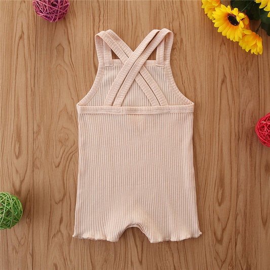 Beige ribbed romper with crossed straps on a wooden surface with decorative elements.
