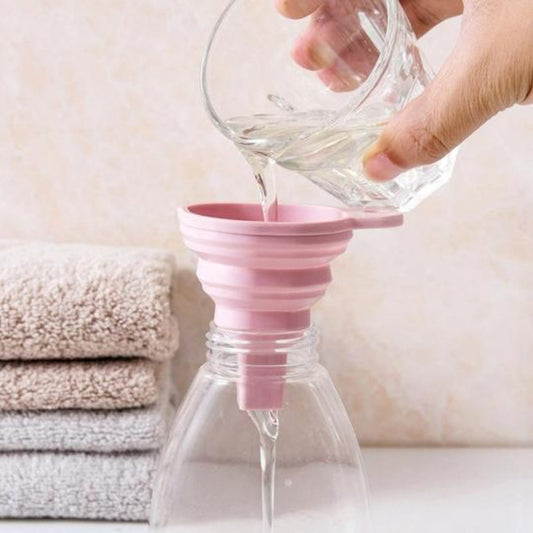 Pink silicone funnel being used to pour liquid into a clear bottle with towels in the background.