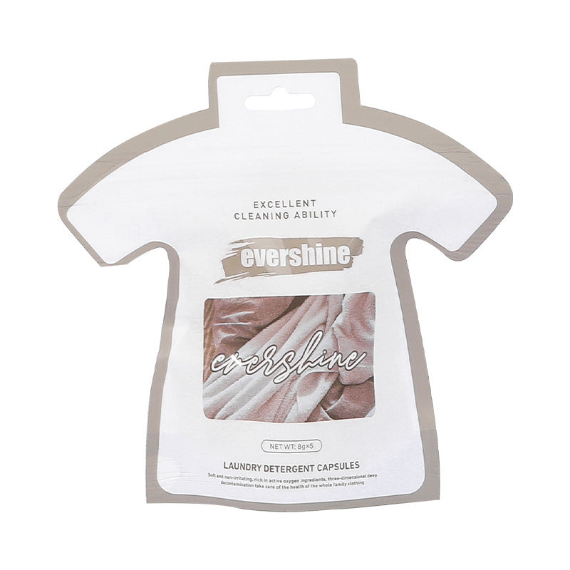 Packaging of laundry gel beads in the shape of a shirt placed on a washing machine, with plants and laundry in the background.