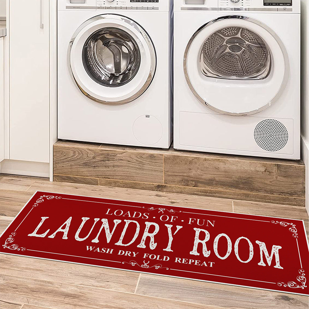 A rectangular black rug with white text and decorative elements, placed on the floor in front of a washing machine and a dryer.
