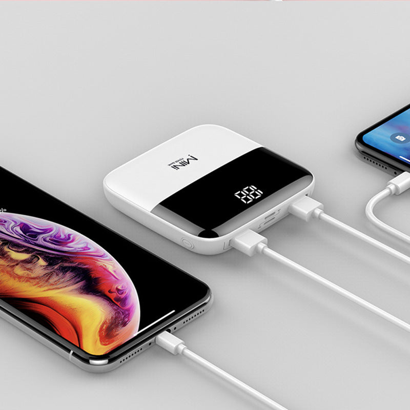 White power bank with digital display connected to a smartphone on a light gray background