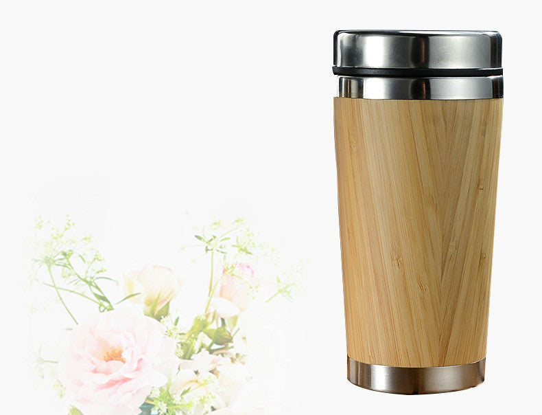 Two bamboo coffee cups with stainless steel lids on a dark surface, one cup is standing upright and the other is lying down showing the interior.