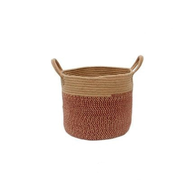 A beige and brown hemp rope laundry storage basket with handles, containing laundry items and placed next to a pillow and a hat on a white furry surface.