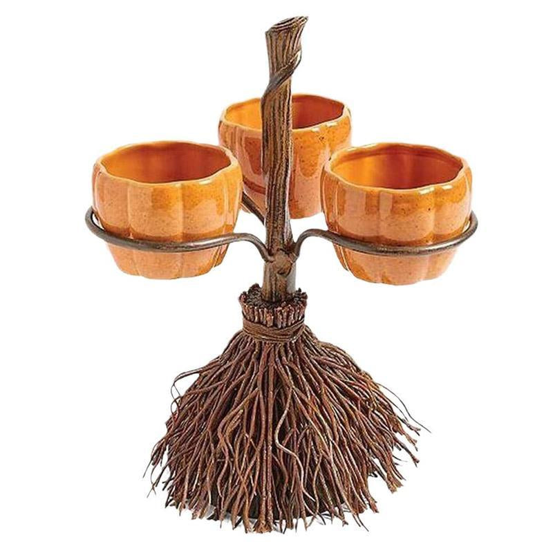 A Halloween-themed snack bowl rack decoration featuring an artificial broom with hanging bowls, set against a backdrop with jack-o-lanterns and string lights.
