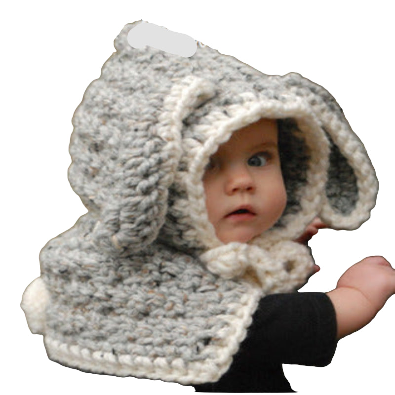 A baby wearing a beige knitted hat with a hood that has a bear face design and wooden button details.