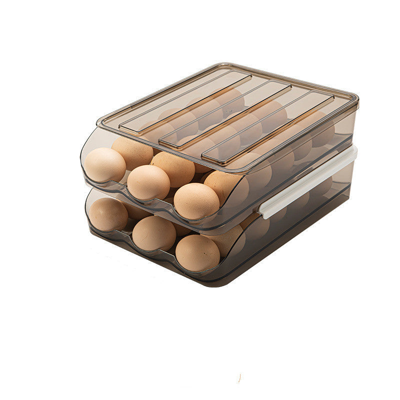 A transparent plastic egg storage box with multiple layers, containing eggs. The box is placed on a kitchen countertop with a whisk in the background.